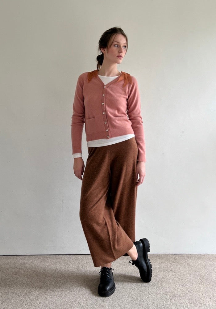 White female model wears dusty pink V neck cashmere cardigan and cashmere pants in cognac colour. 