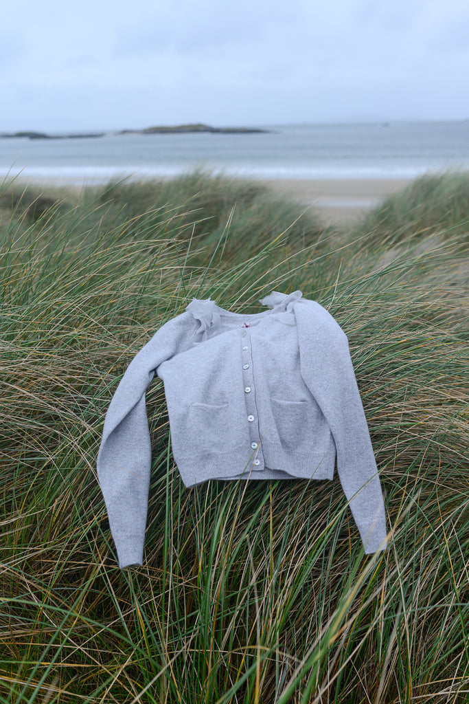 Grey cardigan with mother of pearl buttons lying on marram grass at the seashore with beach and sea in the background