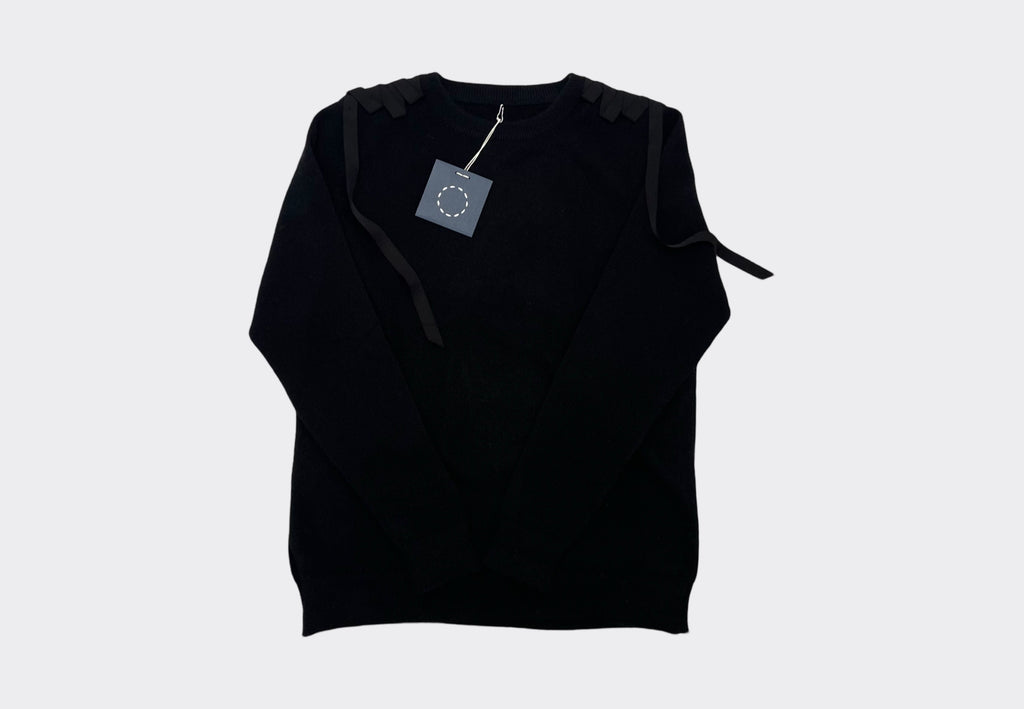 Front product flat lay black cashmere sweater with grosgrain ribbons on shoulders. Navy swing tag with white circle of stitches logo visible 