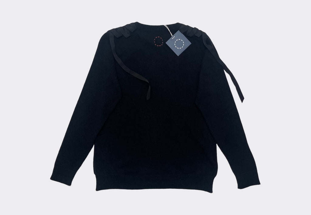 Back product flat lay black cashmere sweater with grosgrain ribbons on shoulders. Navy swing tag with white circle of stitches logo visible 
