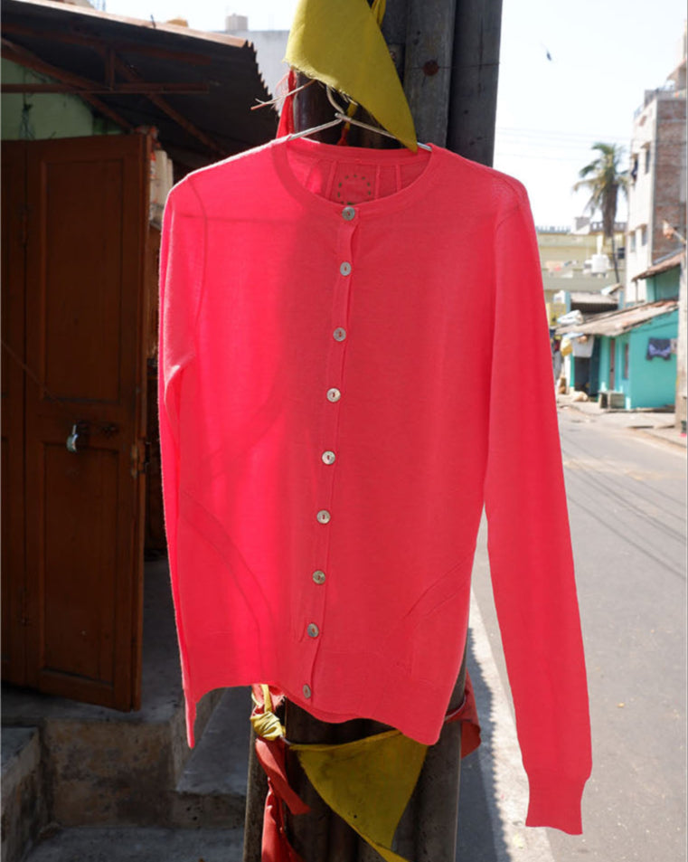 Coral round neck cashmere blend cardigan with buttons hanging from a lamppost with yellow flags against Indian backdrop
