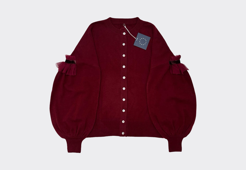 Deep burgundy red round neck cardigan with light coloured buttons, dropped shoulder and bulbous lower sleeves with tulle velvet detail on a light gray background