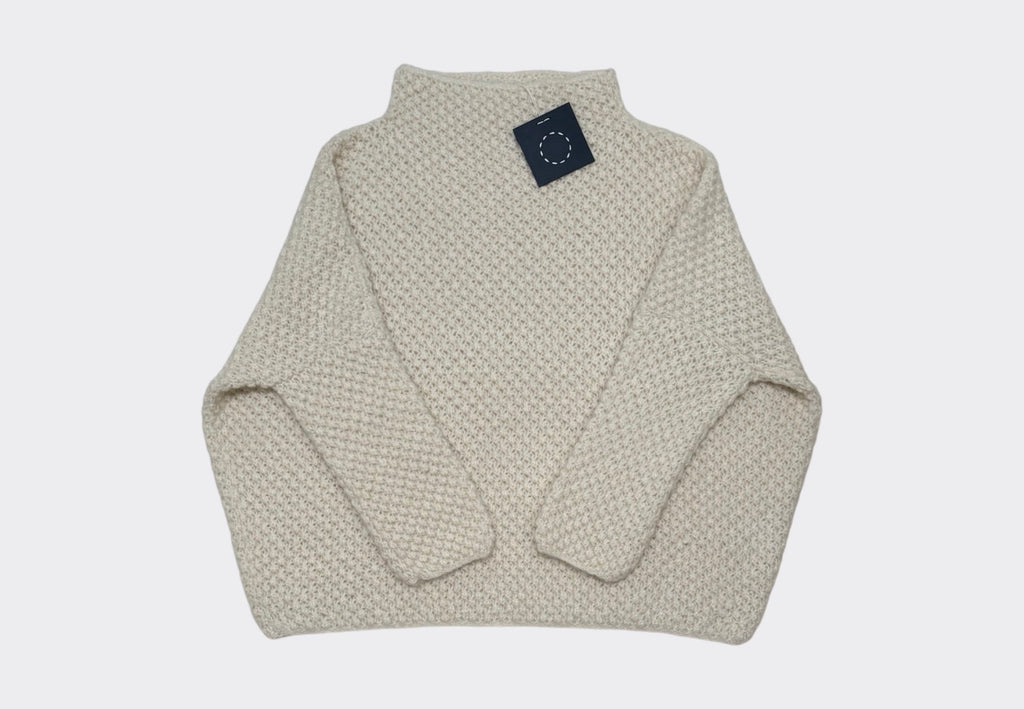 A beige, hand knit sweater with a complex stitch pattern laid flat.