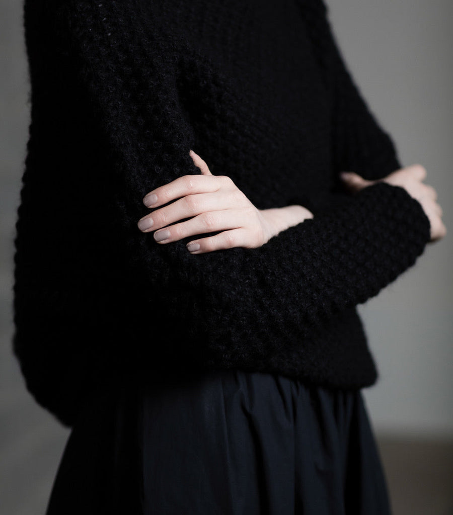 Person wearing a black hand knit textured sweater against a gray background