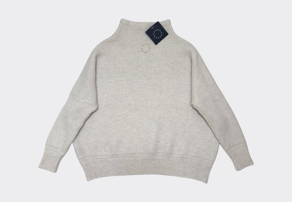 White 5-ply cashmere sweater with a funnel neck, bracelet sleeves, and ribbed hem and cuffs on pale grey background with navy tag and red circle of stitches logo