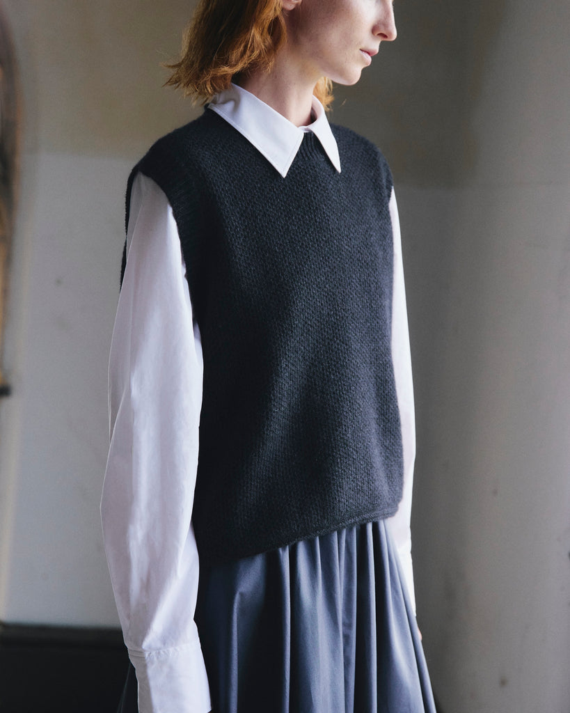 Woman with red hair wearing a dark knitted vest over a white shirt and navy skirt