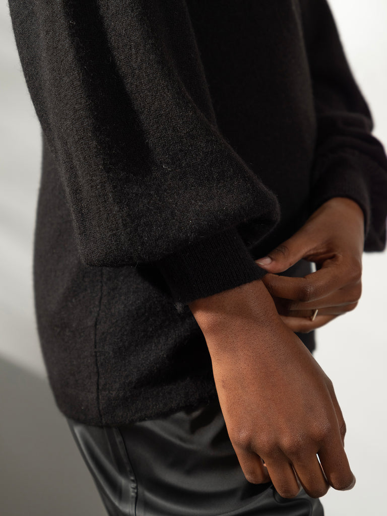 Close up image of dark skinned woman pulling down cuff of black cashmere knit sweater