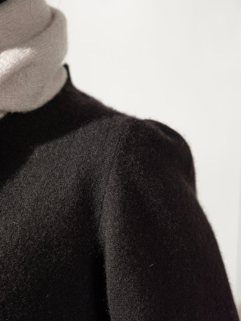 Close up image of shoulder of cashmere knit black sweater witth pale scarf against a white background