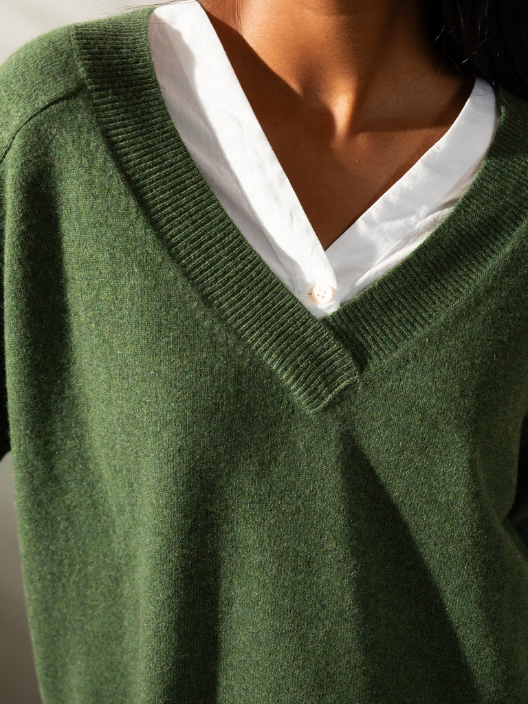 Close up of neck area of woman with dark hair wearing v neck green cashmere knit sweater with white shirt underneath