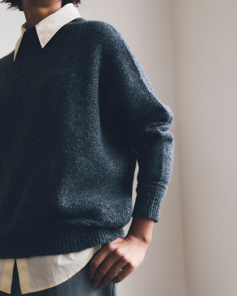 Model wears a Salt and Pepper Harris Tweed oversized Skellig cashmere sweater with dropped shoulder and ribbed sleeve and hem worn over a yellow shirt her thumb hooked into her pocket of grey trousers